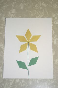 a flower made out of paper sitting on top of a sheet of white paper with yellow and green leaves