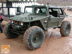 an army vehicle parked in the mud with people standing around it and tents behind it