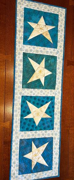 a quilted wall hanging on the side of a wooden floor with three white stars