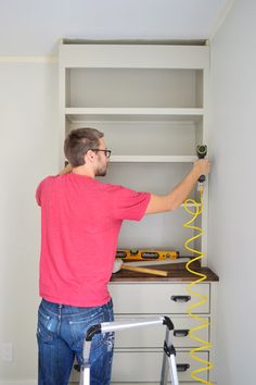 a man in pink shirt and blue jeans standing next to a white shelf with tools on it