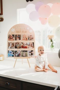 a baby sitting on top of a counter in front of a sign with photos and balloons