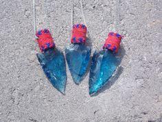 three pieces of glass with red and blue beads hanging from them on a chain in the sand