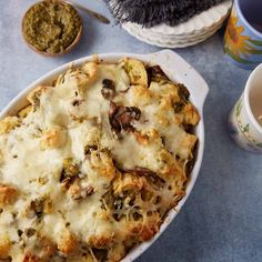 a casserole dish with meat and vegetables in it next to two cups of coffee