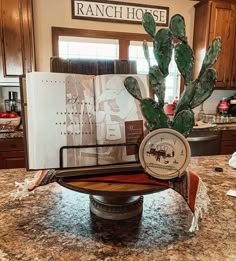 a kitchen counter top with a clock and cactus on it's stand in front of an open cookbook