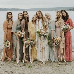 a group of women standing next to each other on a beach holding bouquets and flowers