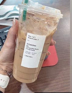 a woman holding a cup of iced coffee in front of a computer keyboard and mouse