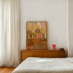 a bed with white sheets and a painting on the wall above it next to a window