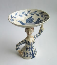 a ceramic figurine holding a blue and white plate on its head with leaves