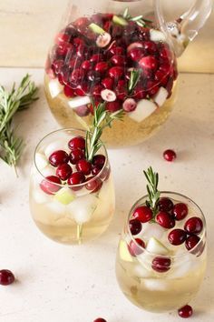 two glasses filled with ice and cranberries on top of a white countertop