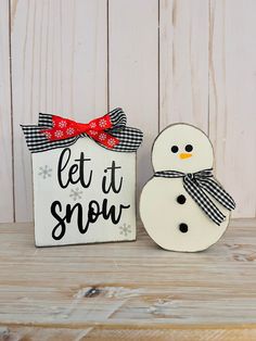 two snowmen are sitting next to a sign that says let it snow with a red bow