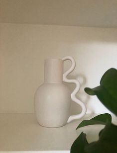 a white vase sitting on top of a table next to a green leafy plant