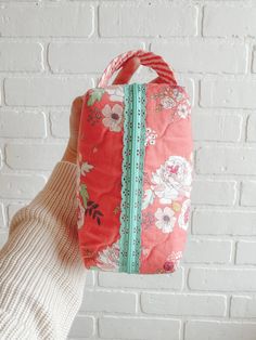 a person holding up a red and green flowered handbag against a white brick wall