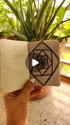 someone is holding up an open book in front of a potted plant with leaves