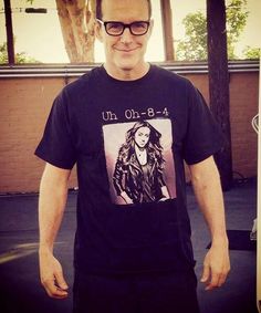 a man with glasses standing in front of a building wearing a t - shirt that says uh 0 3 4