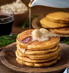 a stack of pancakes with syrup being poured on top and topped with maple syrup, sitting on a wooden plate