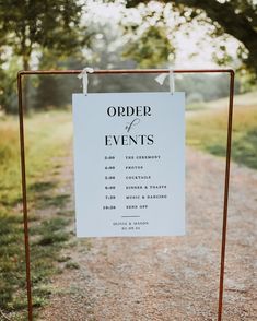 a sign that says order of events hanging from a rusted metal frame on the side of a dirt road