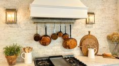 pots and pans are hanging on the wall above an oven in a kitchen with white brick walls