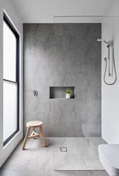 a modern bathroom with concrete walls and floor, along with a wooden stool in the foreground