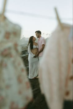 a man and woman standing next to each other in front of dress hanging on a clothes line