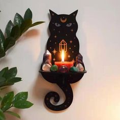 a candle that is sitting on a shelf next to some plants and a cat figurine