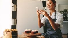 a woman sitting at a table with cupcakes and looking at her cell phone