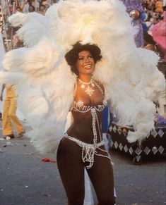 a woman in a costume is walking down the street with large white feathers on her head