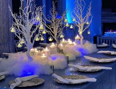 the table is set with candles, plates and snow - covered trees in white lights