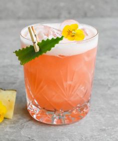 a pink drink with yellow flowers on the rim and green leafy garnish