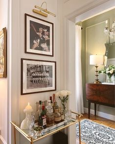 a bar cart with liquor bottles on it in front of two framed pictures and a chandelier