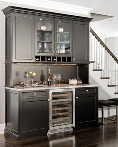 a kitchen with gray cabinets and wine glasses on the counter top, next to stairs