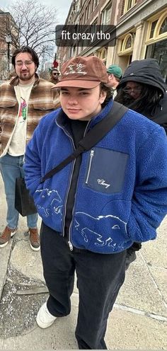 a man in a blue jacket and hat standing on the sidewalk with other people behind him