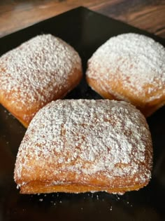 three powdered sugar donuts on a black plate