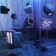 several televisions and monitors are in a room with wires hanging from the ceiling above them