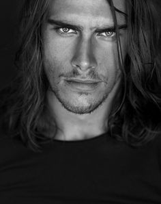 a black and white photo of a man with long hair looking at the camera while wearing a t - shirt