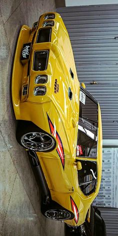 the rear end of a yellow sports car hanging on a wall in front of a garage door