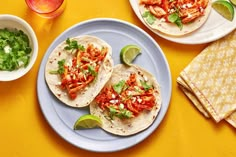 three tacos are sitting on a plate with limes and cilantro