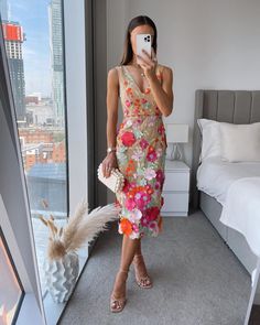 a woman taking a selfie with her phone in front of a window, wearing a floral dress