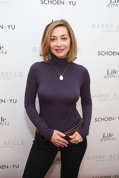 a woman standing in front of a white wall wearing black pants and a purple top