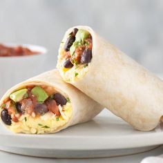 two burritos on a plate with salsa and avocado in the background