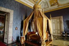 a canopy bed in the middle of a room with blue walls and gold trimmings