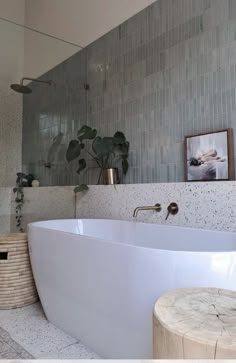 a large white bath tub sitting next to a wooden stool in a bathroom with tiled walls