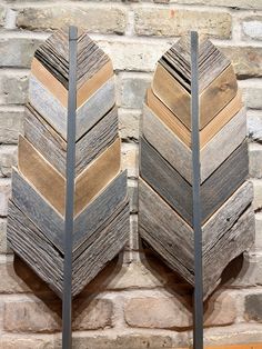 two decorative wooden arrows are on display against a brick wall, one is made out of wood and the other is metal