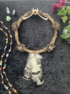 a feather and beaded necklace on display next to other beads, stones and flowers