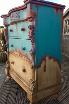 an old dresser painted blue and brown with rust on the bottom drawer, sitting on a wooden deck