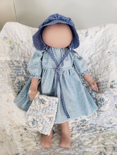 a doll is laying on a bed with a blue dress and bonnet over it's head