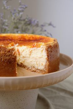 a cheesecake on a plate with a piece missing from the cake and flowers in the background