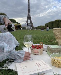 a woman sitting on the grass with a book and glass of wine in front of the eiffel tower