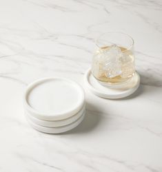 three white plates and a glass on a marble counter top with ice cubes in the middle