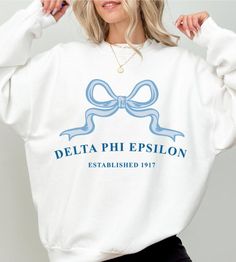 Soft, cute, and trendy, this Delta Phi Epsilon sorority ribbon crewneck will quickly become your go-to cozy sweatshirt! Use the drop down to specify preference between white, ash, sand, light blue, or light pink.  LISTING IS FOR DELTA PHI EPSILON. Please be sure you are ordering for your correct Sorority.  We print on high quality, soft, & heavyweight materials, sustainably made and printed in the US. ♥ SIZING ♥ Unisex Sizing- For a more feminine, fitted look we recommend getting your size. For Alpha Phi Sorority, Sigma Delta Tau, Theta Phi Alpha, Tri Sigma, Alpha Sigma, Alpha Sigma Alpha, Zeta Tau Alpha, Alpha Chi Omega, Alpha Chi