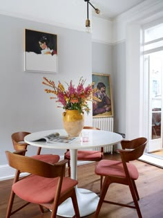 a white table with four chairs and a vase filled with flowers on top of it